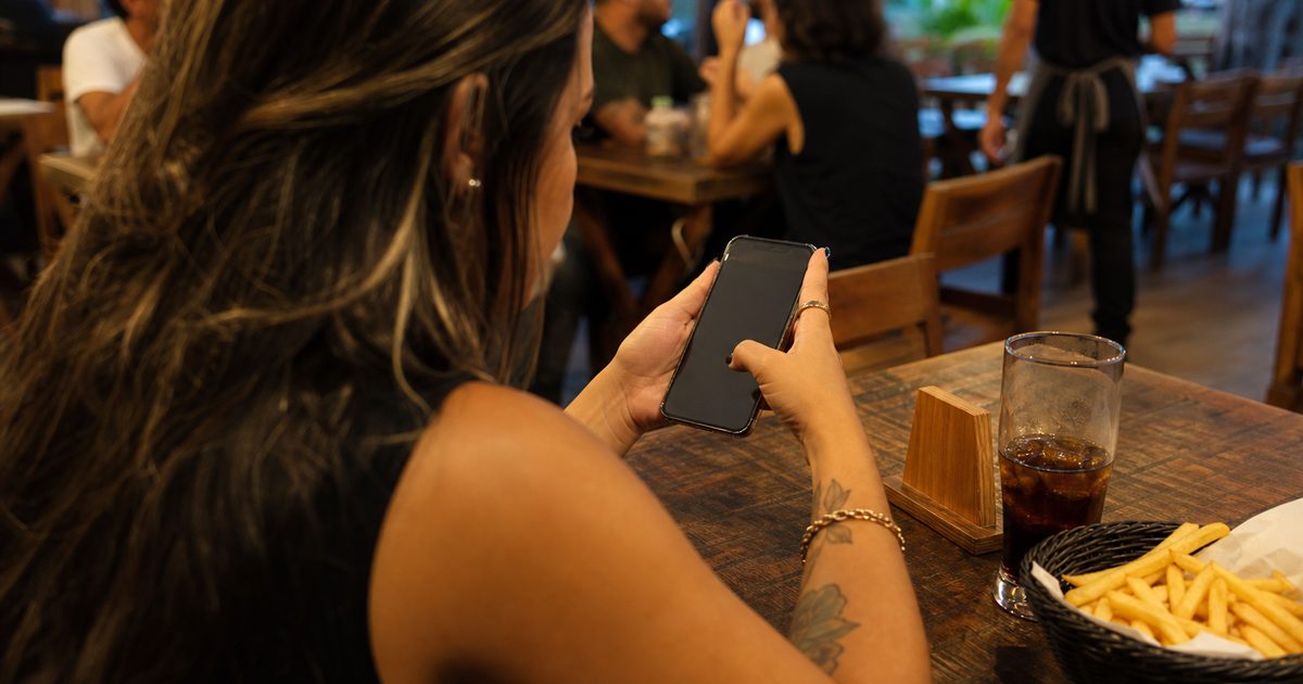 Cliente sentado à mesa de um restaurante escolhendo o pedido no celular pelo cardápio QR Code na mesa